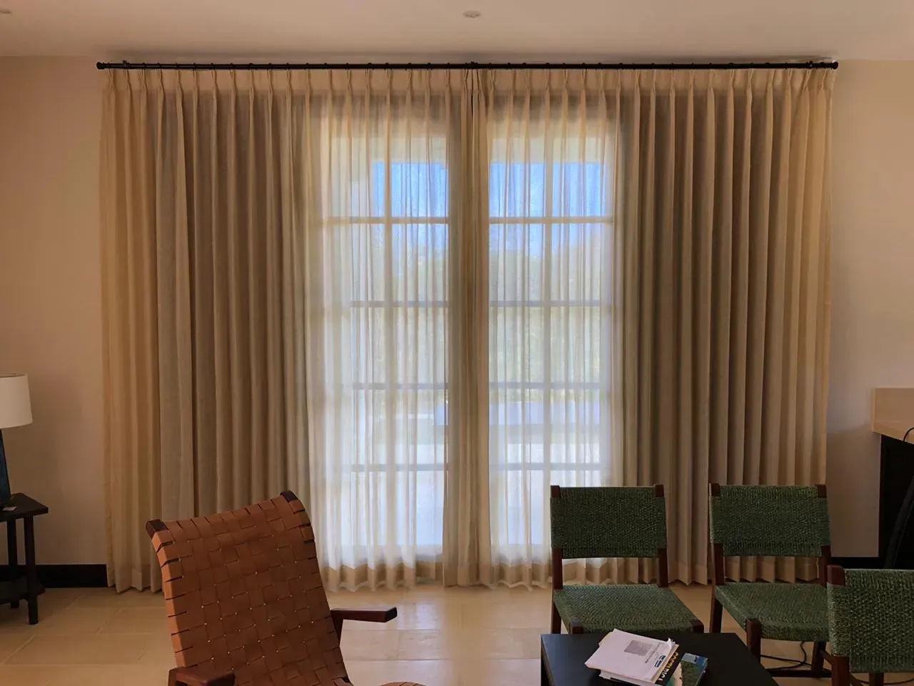 Visillos beige de piso a techo con paneles laterales y pliegue pinzado en una sala.