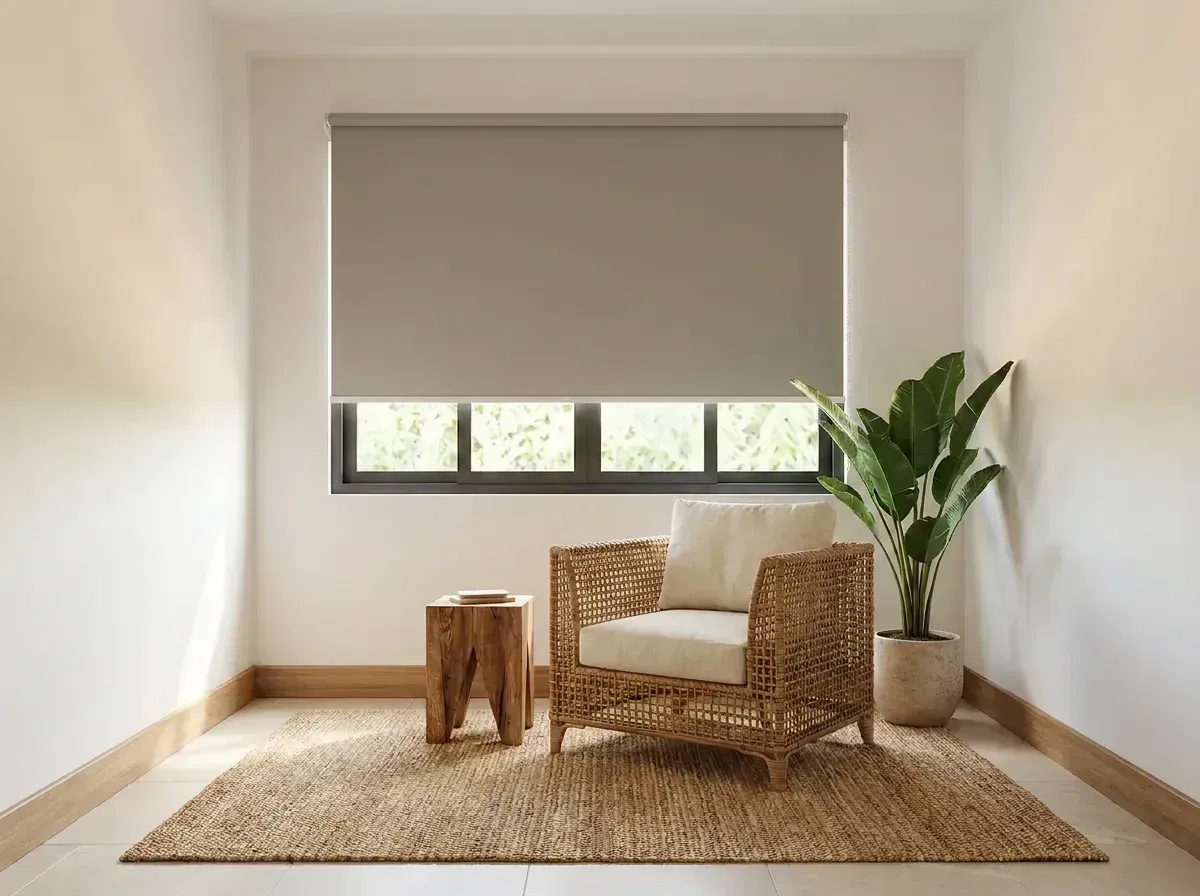 Rincón de estar con la cortina Día y Noche bajada sobre la ventana, butaca de fibra natural, mesa auxiliar de madera y alfombra de yute.