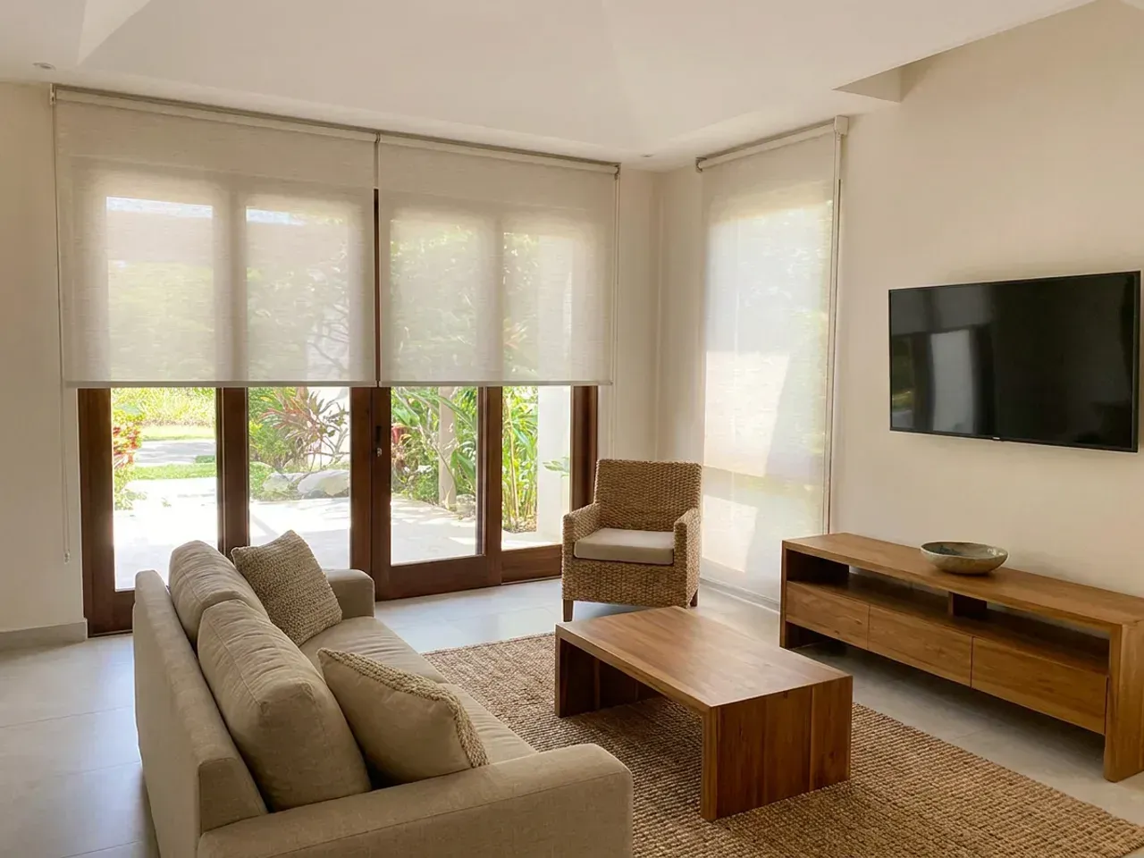 Sala con dos ventanales cubiertos por cortinas Día y Noche, sofá de lino arena, mesa de centro de madera maciza y mueble bajo de teca.