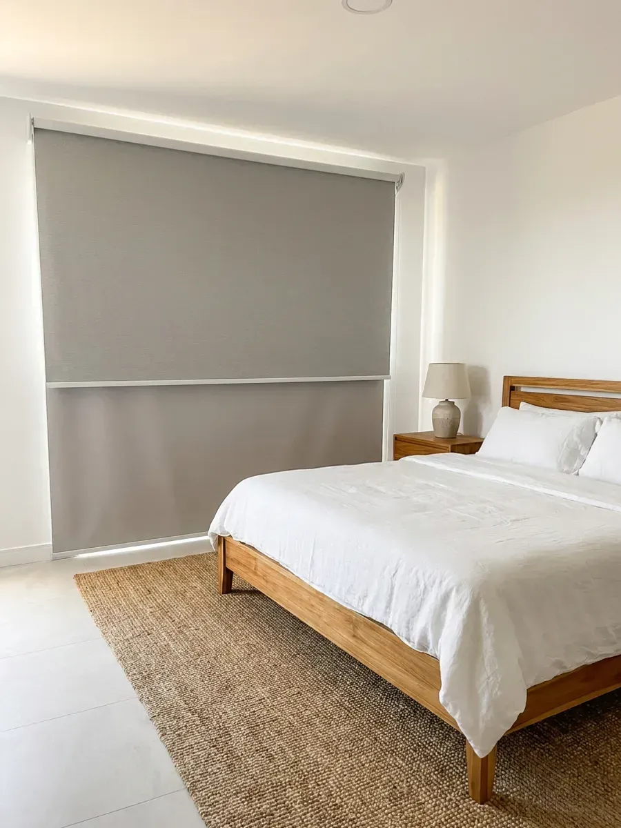 Dormitorio con el sistema Día y Noche cubriendo el vano de pared a pared, cama de madera clara con ropa de cama blanca y alfombra de fibra natural.