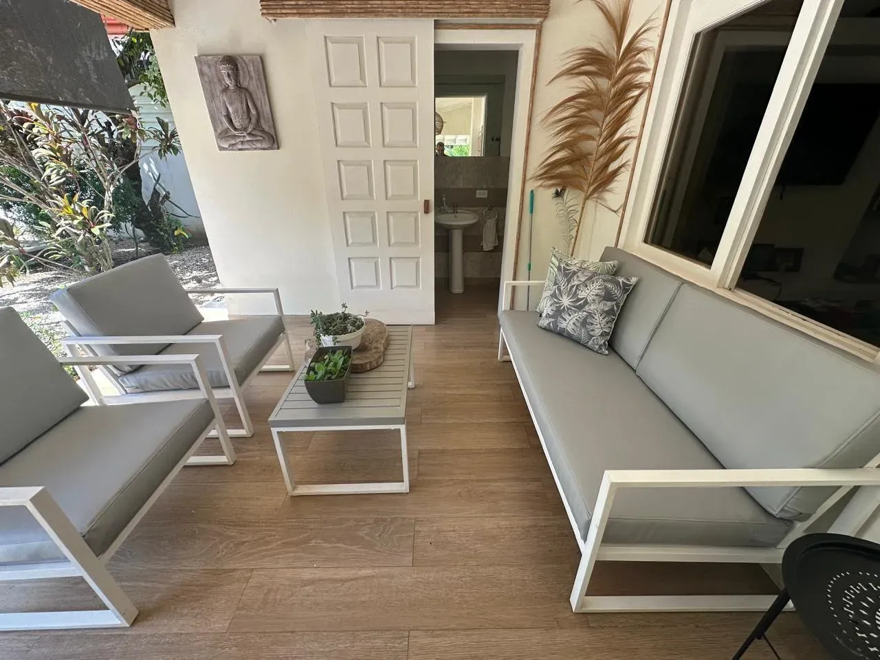 Área lounge exterior con sofá y sillones blancos modulares de cojines beige sobre piso de madera.