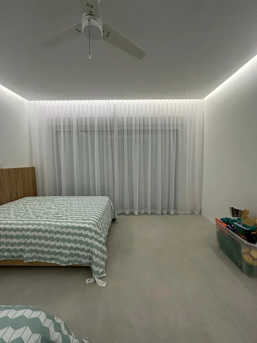 Recámara con cortinas vaporosas blancas piso a techo, ventilador de techo y cabecero de madera.