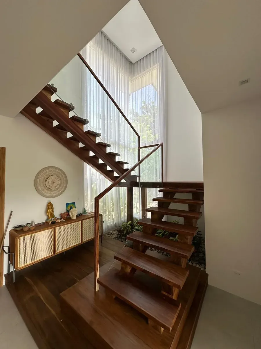Cortinas vaporosas blancas de doble altura junto a escalera flotante de madera y barandal de vidrio.
