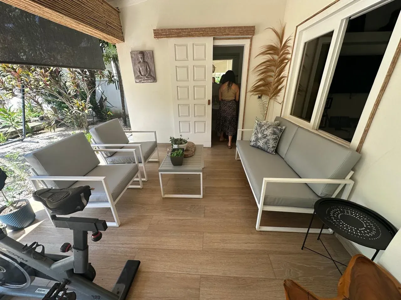 Terraza cubierta con sofá y sillones modulares blancos de cojines beige sobre piso de madera.