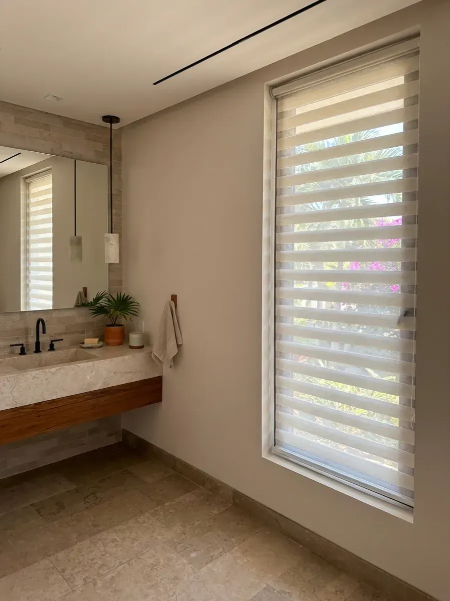 Baño moderno con persiana día y noche blanca, lavabo de concreto y espejo con luz indirecta.
