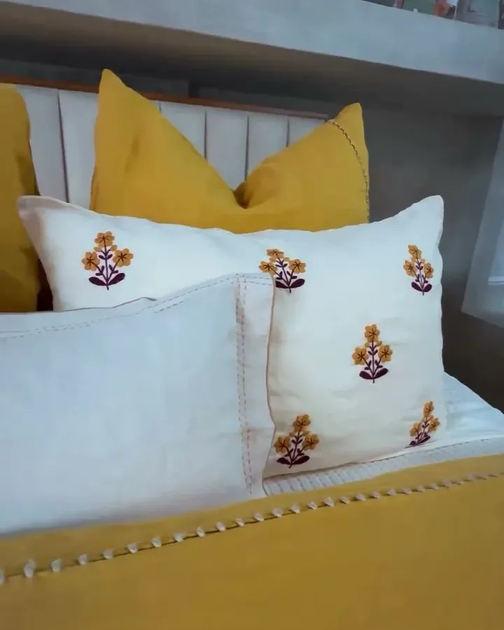 Close-up of the floral-embroidered pillows and the openwork trim of the yellow duvet.