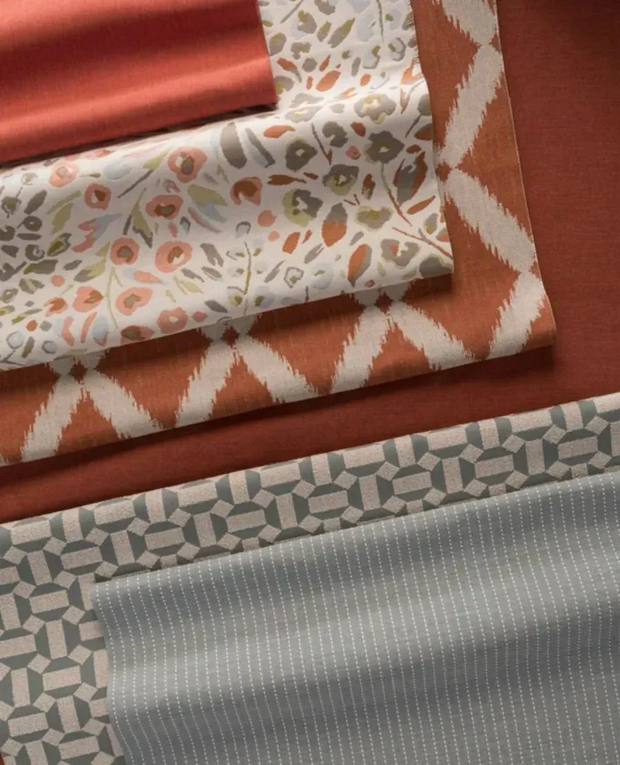 Telas de tapicería dobladas en tonos terracota, arena y gris, con estampados florales y geométricos.