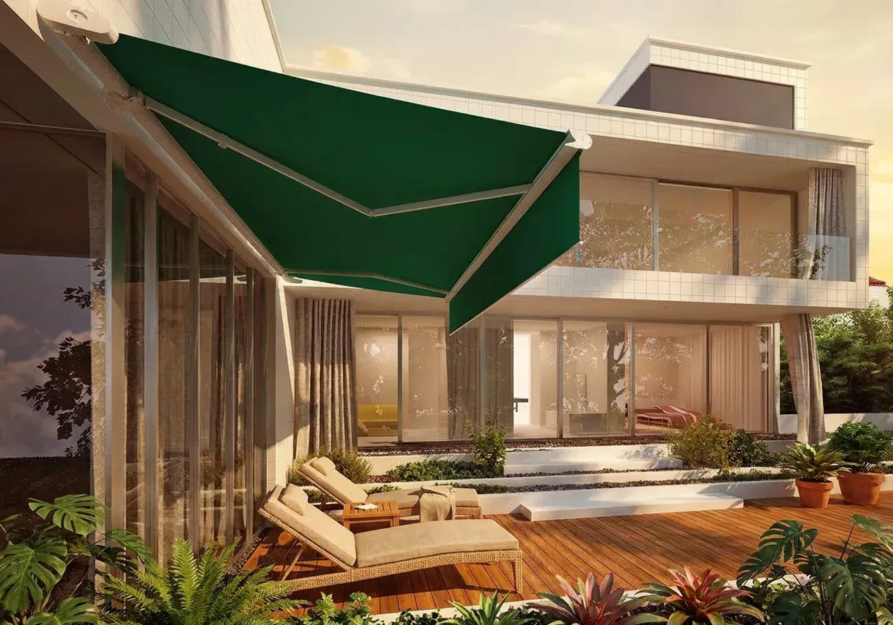 Toldo de brazo extensible en lona verde desplegado sobre un deck de teca, con tumbonas de lino y vegetación tropical.