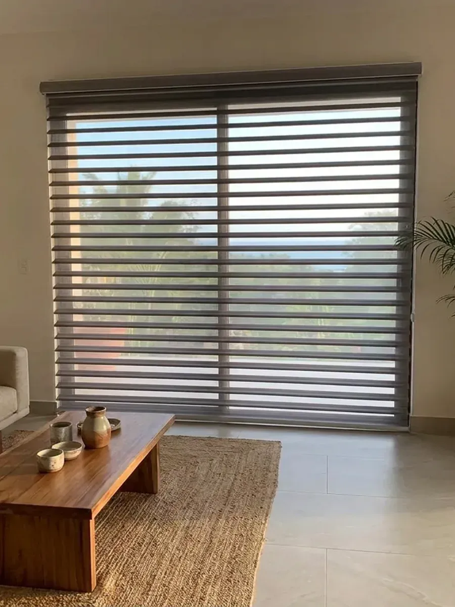 Sala con Triple Shade sobre el ventanal, sofá de lino, mesa de centro de madera y palmera en maceta de barro.