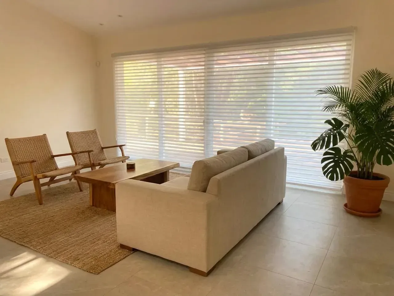 Sala con pared de Triple Shade en posición abierta, sofá de lino, butacas de fibra y alfombra de yute.